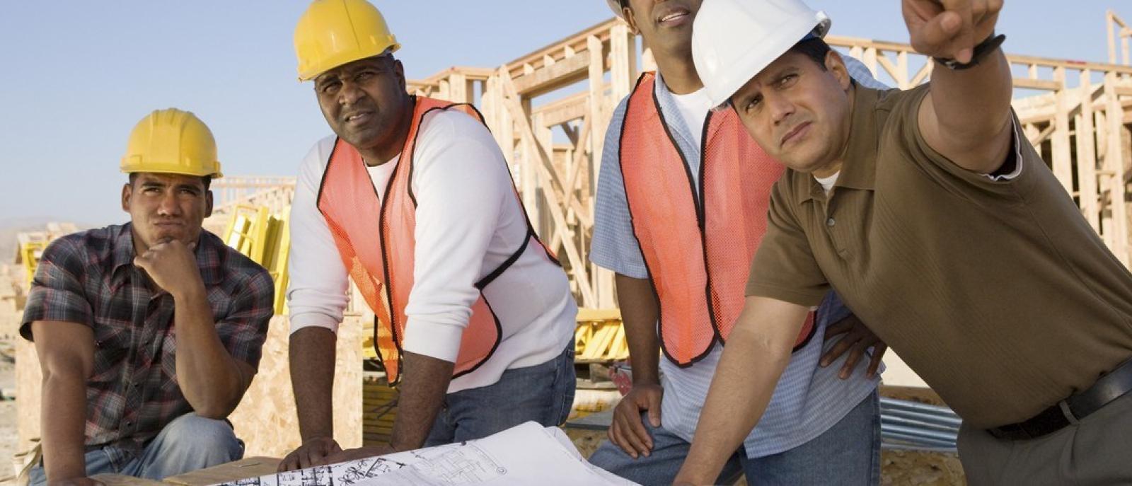Contractors standing together to review blueprints for a new building